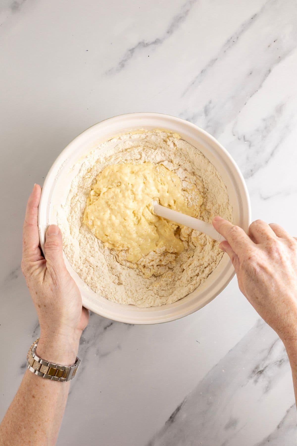 Image showing the wet ingredients being mixed into the dry ingredients with a white spatula.