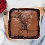 Sourdough chocolate cobbler baked in a square white baking dish. This self saucing pudding is displayed with a bowl of fresh raspberries.