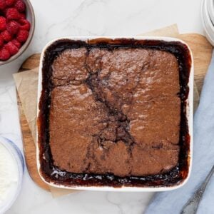 Sourdough chocolate cobbler baked in a square white baking dish. This self saucing pudding is displayed with a bowl of fresh raspberries.