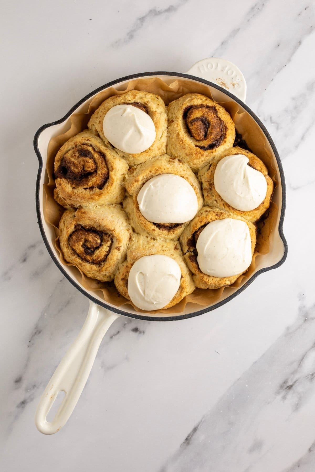 A cast-iron skillet filled with 8 sourdough discard cinnamon rolls. 5 of the rolls have been topped with vanilla cream cheese frosting. 