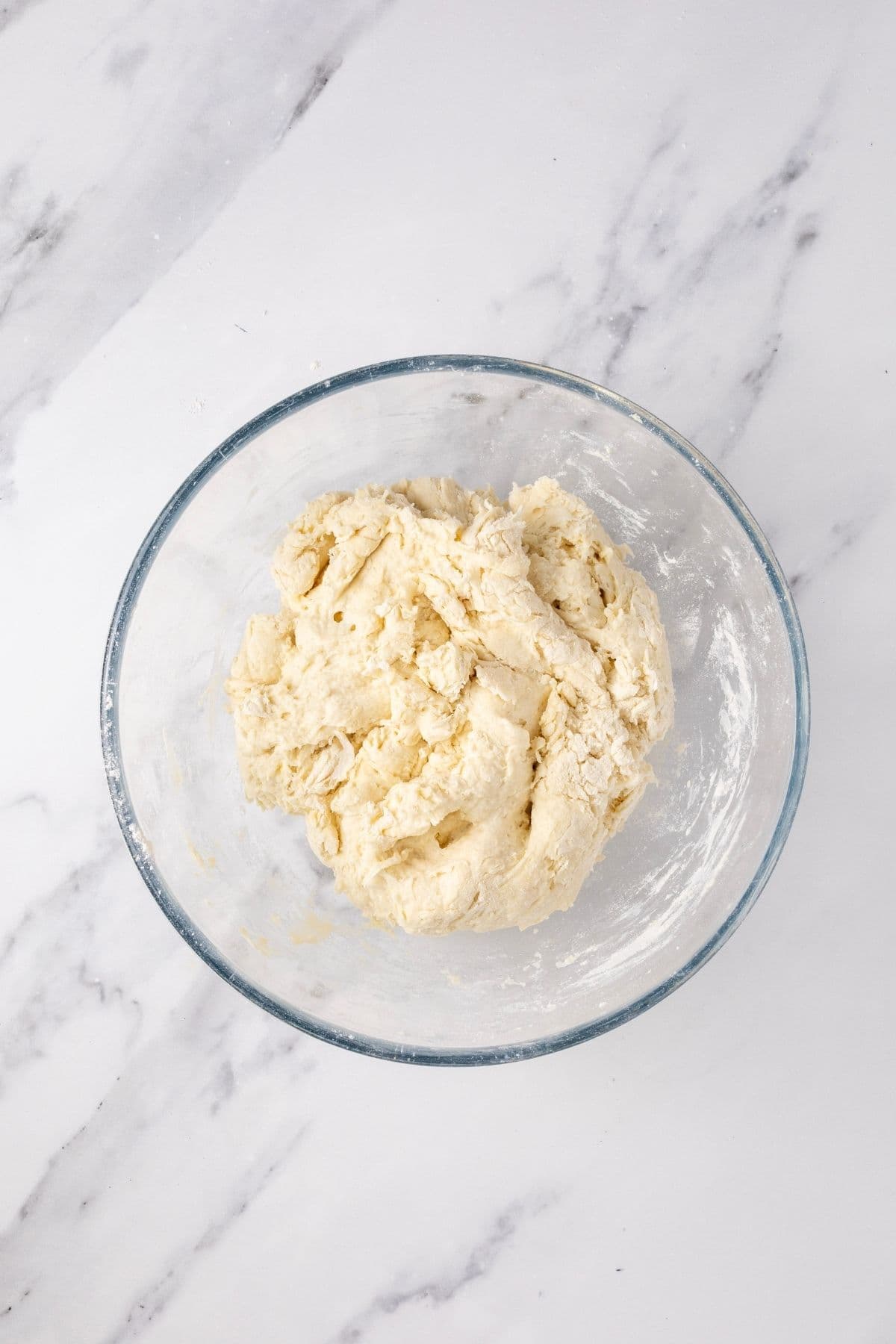 A glass bowl holding a roughly brought together tortilla dough ready to be kneaded.