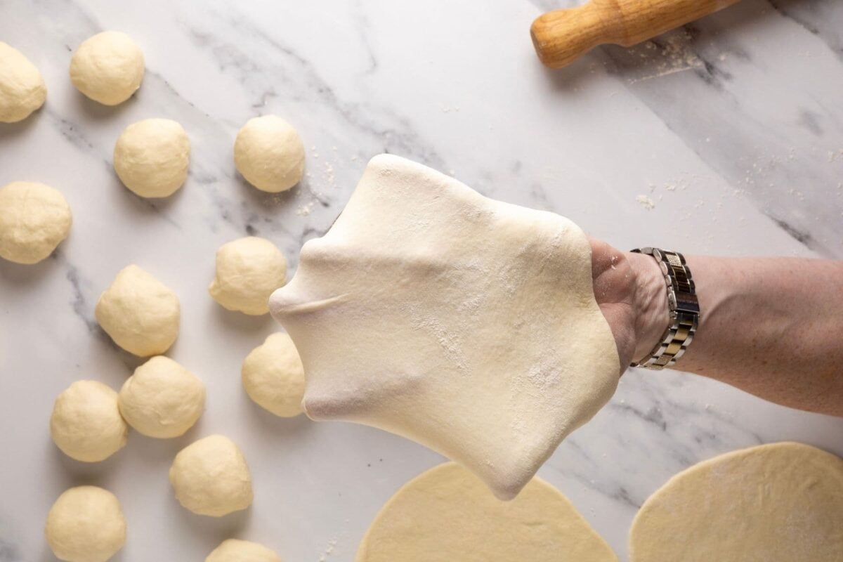 A hand stretching out the dough for a sourdough discard tortilla to show how thin to roll out the dough. You can see the fingers and some light coming through the dough so you can see how thin it is.