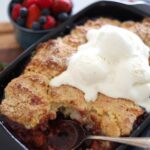 Sourdough berry cobbler baked in a black baking dish and topped with vanilla ice cream.