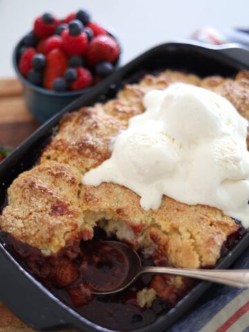 Sourdough berry cobbler baked in a black baking dish and topped with vanilla ice cream.