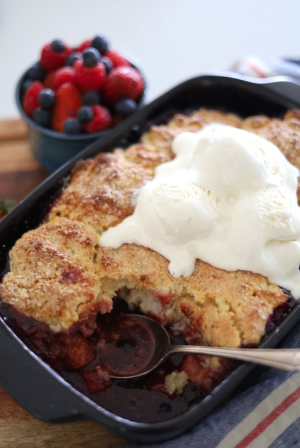 Sourdough berry cobbler baked in a black baking dish and topped with vanilla ice cream.