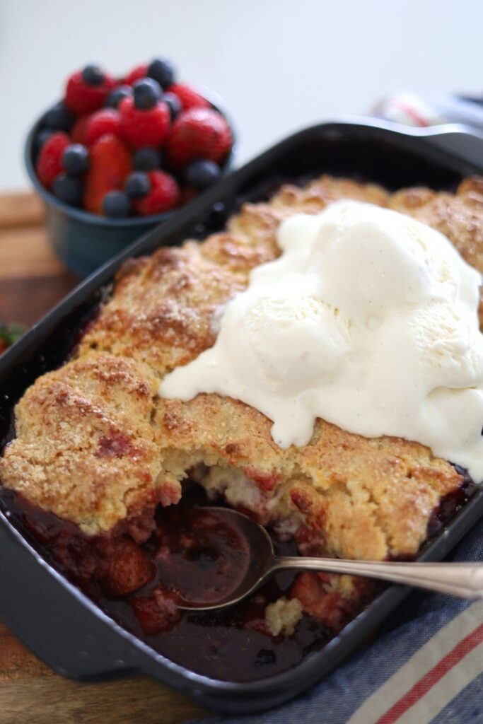 Sourdough berry cobbler baked in a black baking dish and topped with vanilla ice cream.