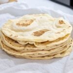 A stack of freshly cooked sourdough discard tortillas nestled in a white flour sack towel.