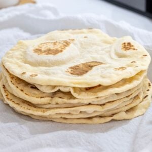 A stack of freshly cooked sourdough discard tortillas nestled in a white flour sack towel.