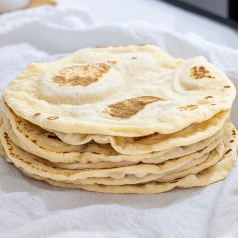 A stack of freshly cooked sourdough discard tortillas nestled in a white flour sack towel.