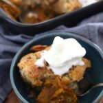 A blue pottery bowl containing a serve of sourdough pumpkin pecan cobbler topped with vanilla ice cream.