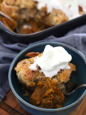 A blue pottery bowl containing a serve of sourdough pumpkin pecan cobbler topped with vanilla ice cream.