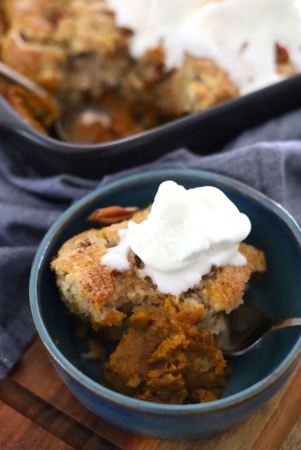 A blue pottery bowl containing a serve of sourdough pumpkin pecan cobbler topped with vanilla ice cream.