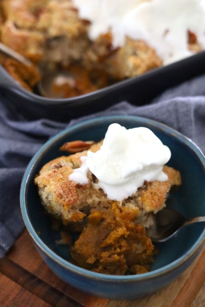 A blue pottery bowl containing a serve of sourdough pumpkin pecan cobbler topped with vanilla ice cream.