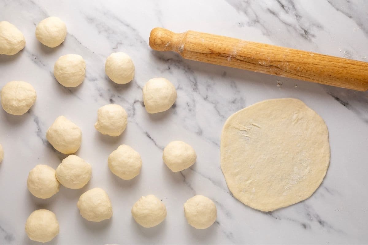 Sourdough tortilla dough balls that have been rounded into small balls. There is one tortilla that has been rolled out really thin.