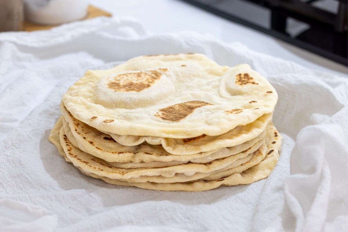 A stack of freshly cooked sourdough discard tortillas nestled in a white flour sack towel.