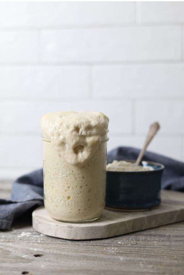 Jar of sourdough starter that has peaked and overflowed down the side of the jar.