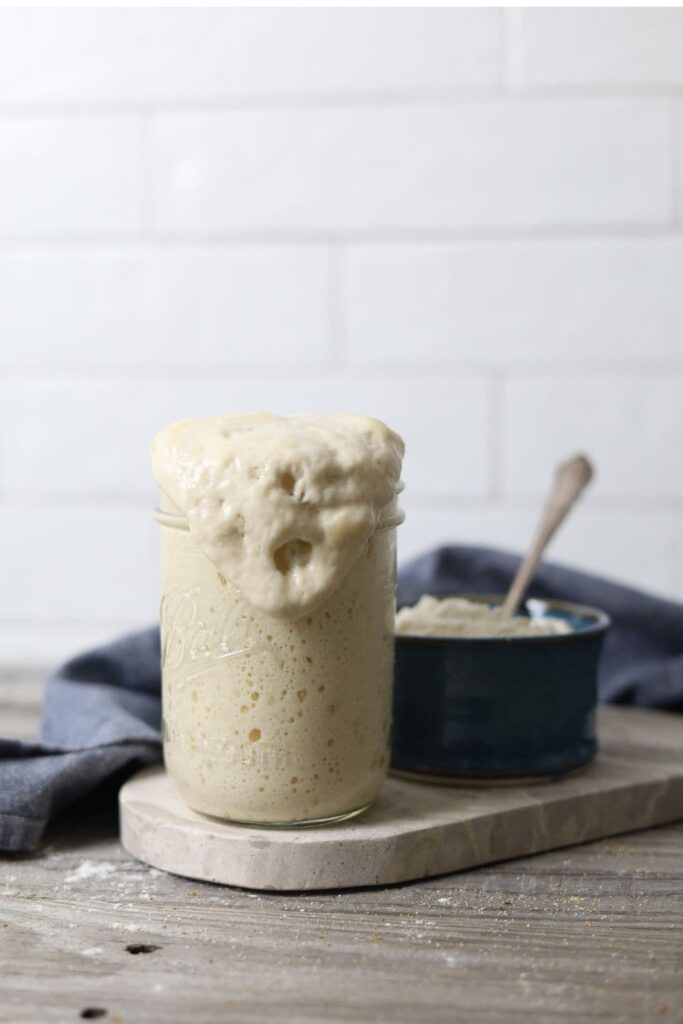 Jar of sourdough starter that has peaked and overflowed down the side of the jar.