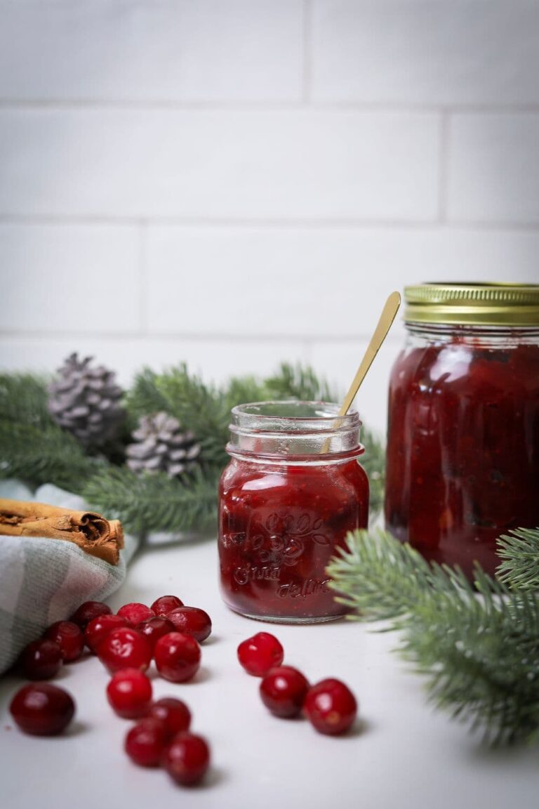 A jar of Christmas chutney nestled amongst frosted pine branches and cranberries.