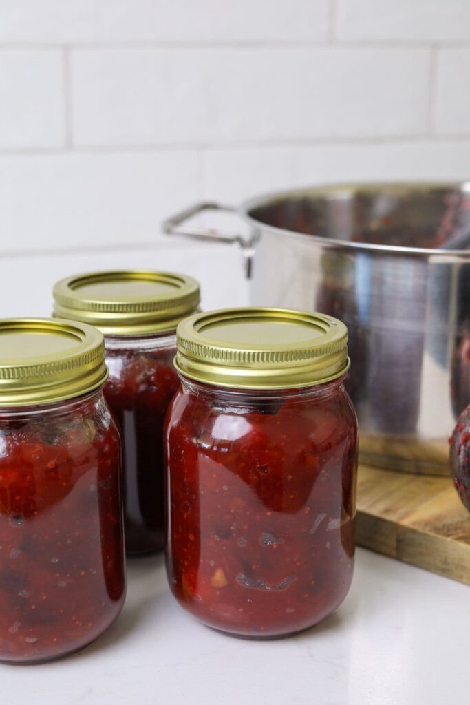 3 jars of Christmas chutney with gold lids sitting next to a stainless steel pot.