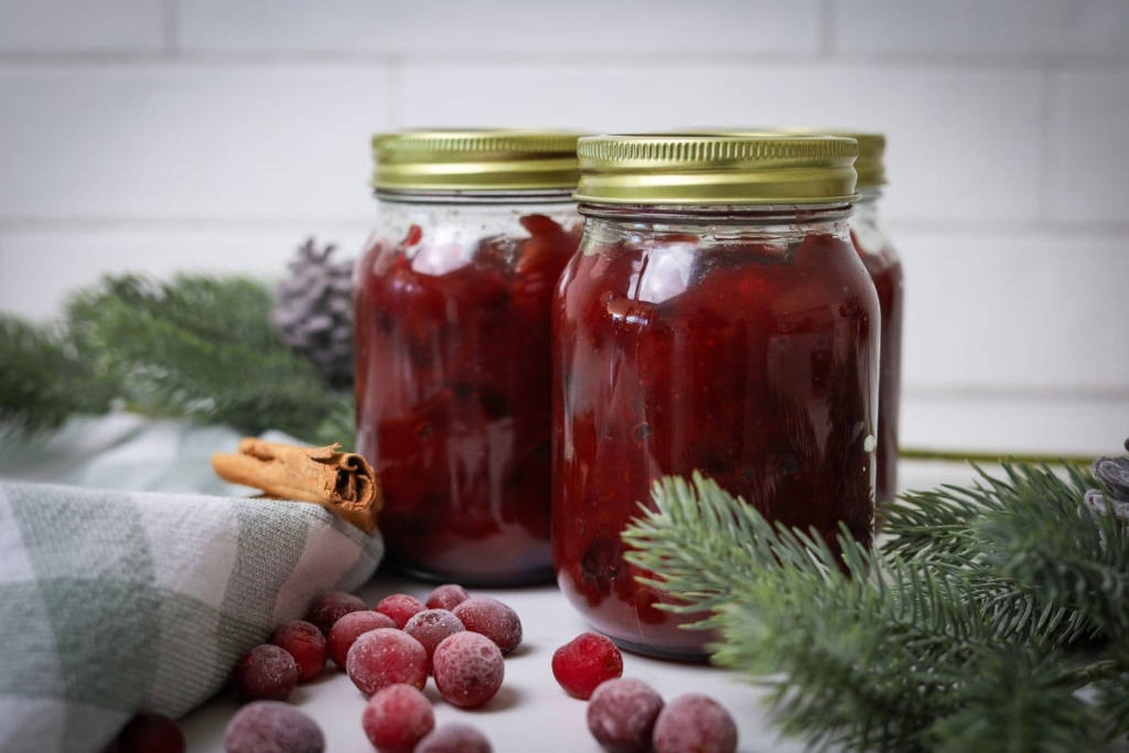 3 jars of Christmas chutney in 500ml jars with gold lids. There are some frozen cranberries and pine branches in the photo for Christmas effects.