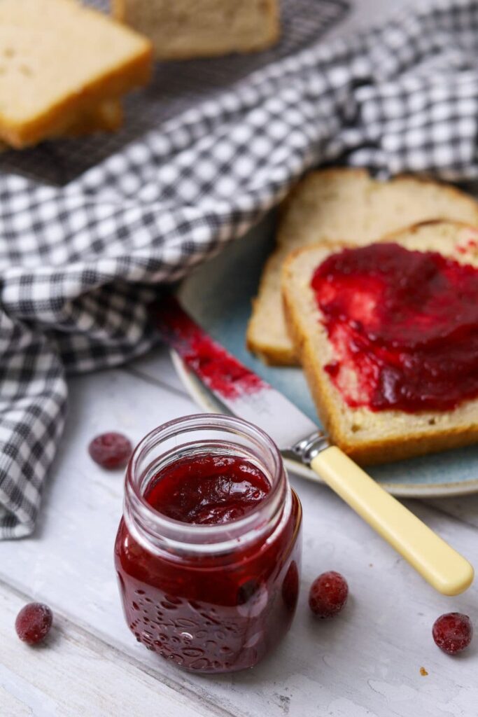 A small jar of cranberry orange jam. You can see a slice of bread spread with the Thanksgiving jam in the background.