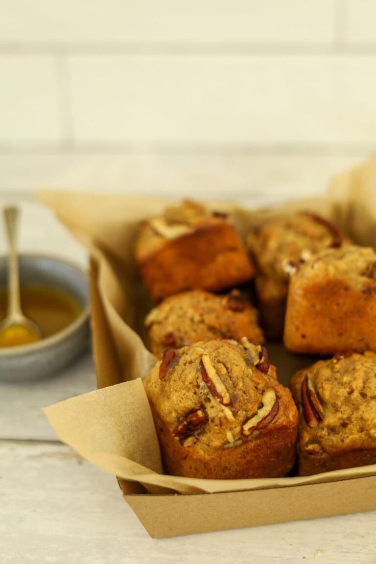 A tray of maple pecan sourdough muffins baked in a square muffin pan. You can see a bowl of maple butter syrup to the left that has been drizzled over the warm muffins.