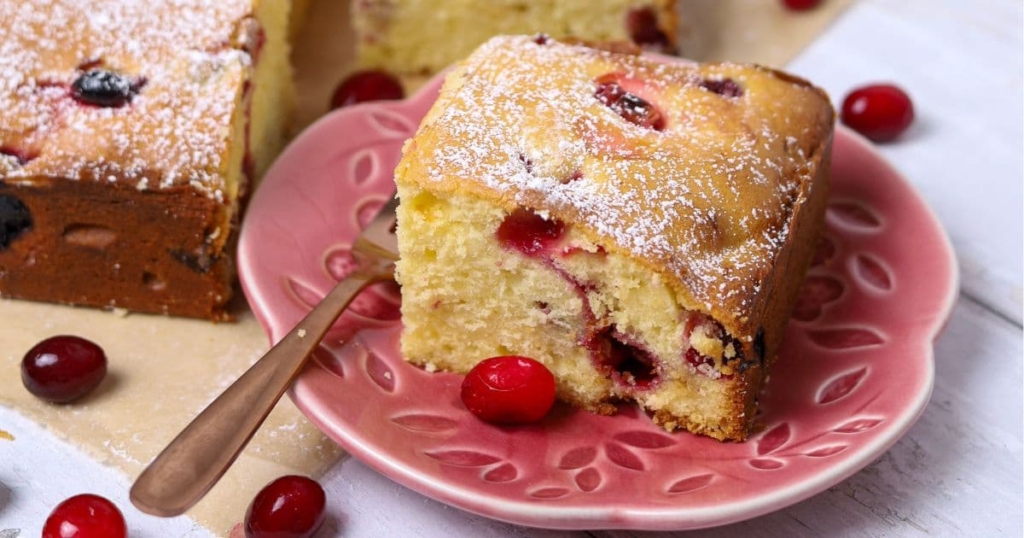 A close up photo of a slice of sourdough cranberry cake sitting on a pink plate.