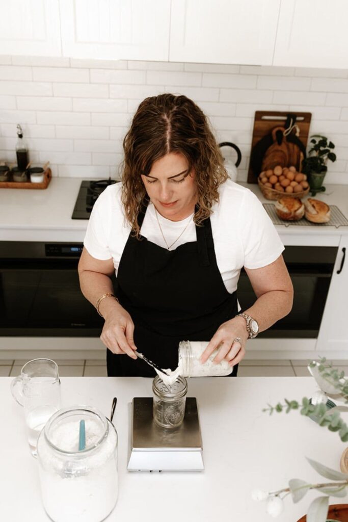 Kate from The Pantry Mama pouring some sourdough starter into an empty jar that is sitting on a set of scales.