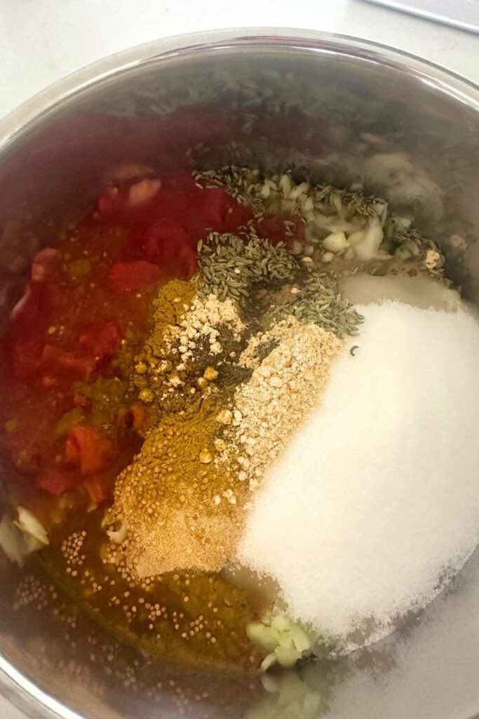 All of the ingredients necessary to make tomato chutney layered into a 5L stainless steel pot.