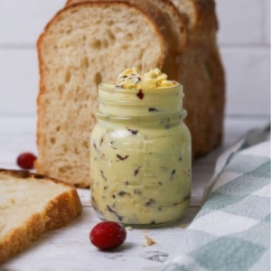 A jar of whipped cranberry orange butter sitting in front of a loaf of sourdough bread.