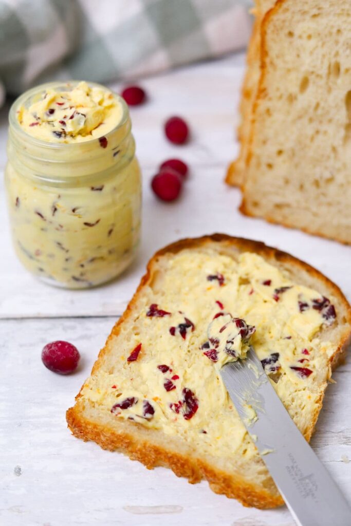 A slice of sourdough bread spread with whipped cranberry orange butter. You can see the jar of cranberry orange butter sitting next to the slice of bread.