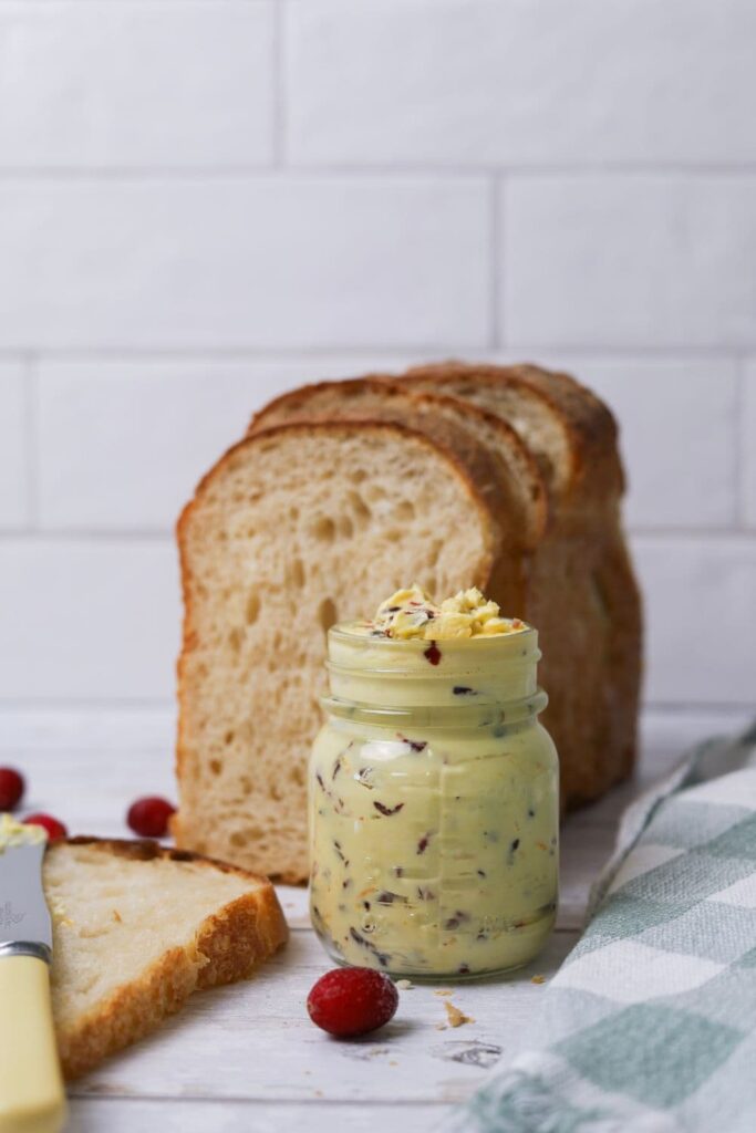 A small jar filled with whipped cranberry orange butter sitting in front of a loaf of sourdough bread.