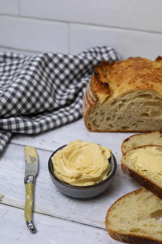 A small bowl of whipped maple butter sitting in front of a loaf of sourdough bread.