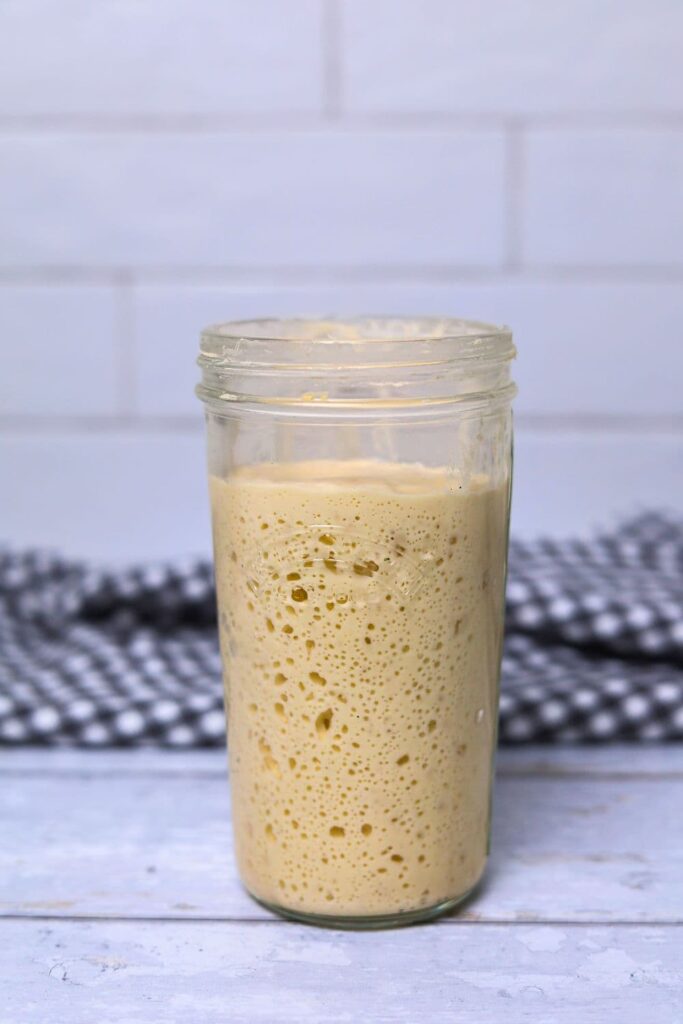 A jar of sourdough starter that has been fed and has risen and is bubbly inside the jar.