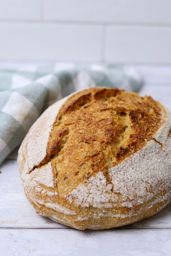 A loaf of 100% whole wheat sourdough bread sitting on a white wooden board.