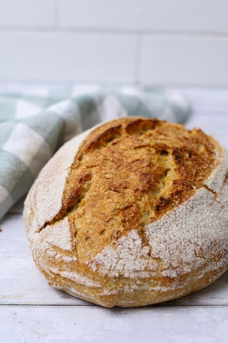 A loaf of 100% whole wheat sourdough bread sitting on a white wooden board.