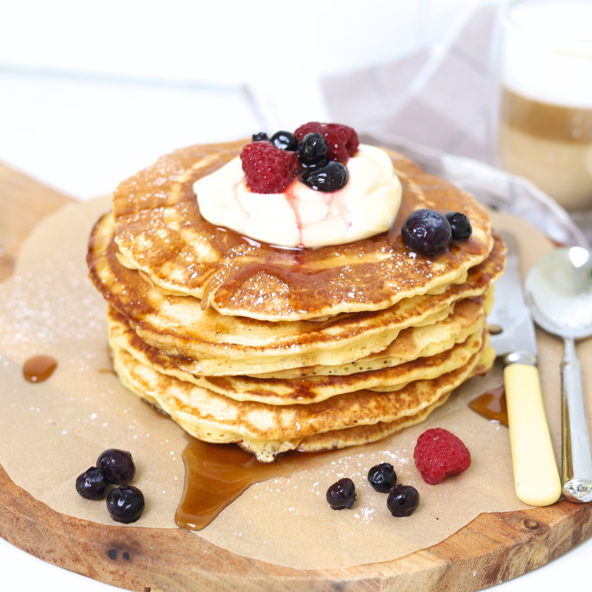 Sourdough breakfast pancakes stacked on a plate, topped with whipped cream, syrup, and fresh berries.