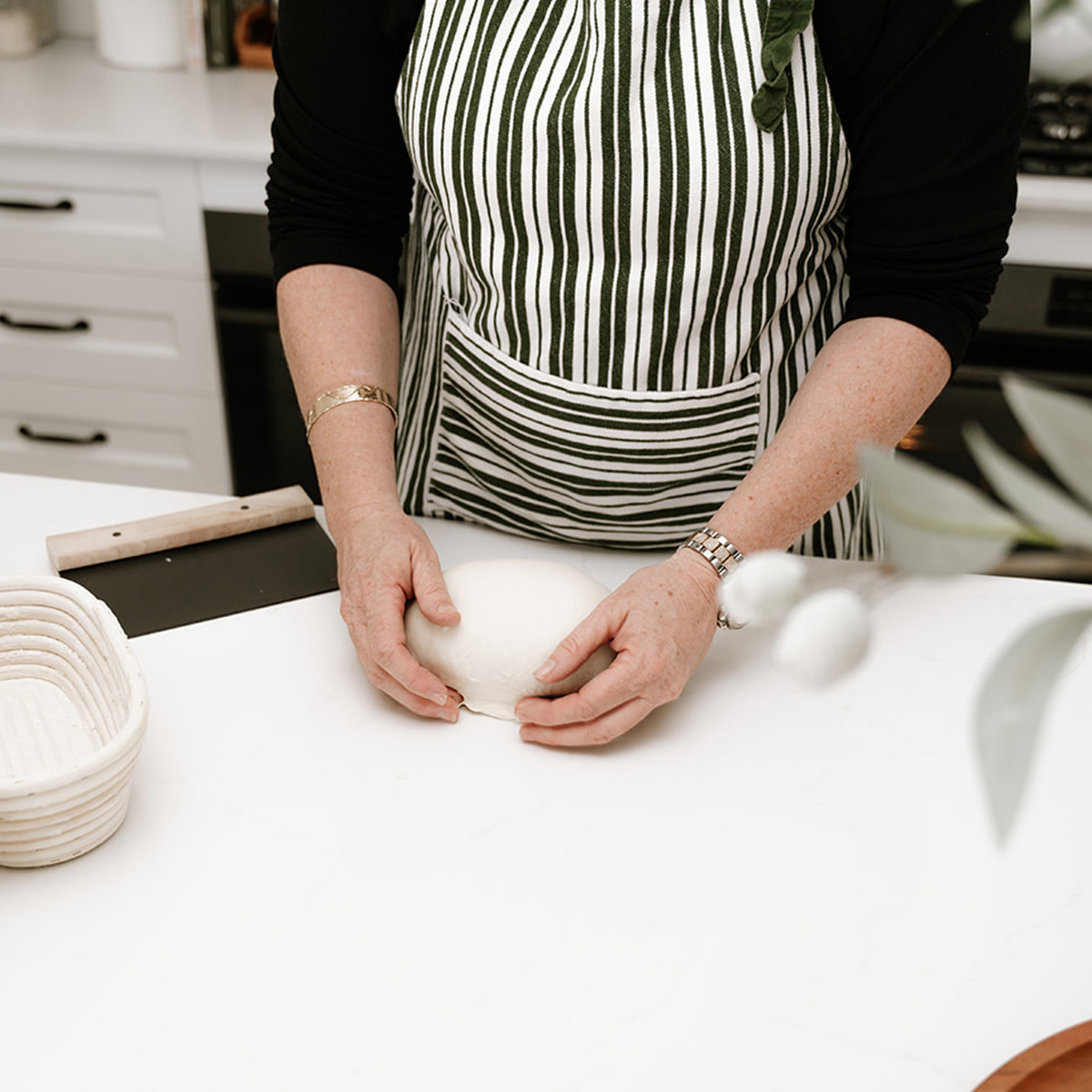 Woman working with a ball of sourdough on a kitchen counter.