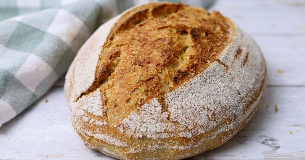 A loaf of 100% whole wheat sourdough bread sitting in front of a green check dish towel.