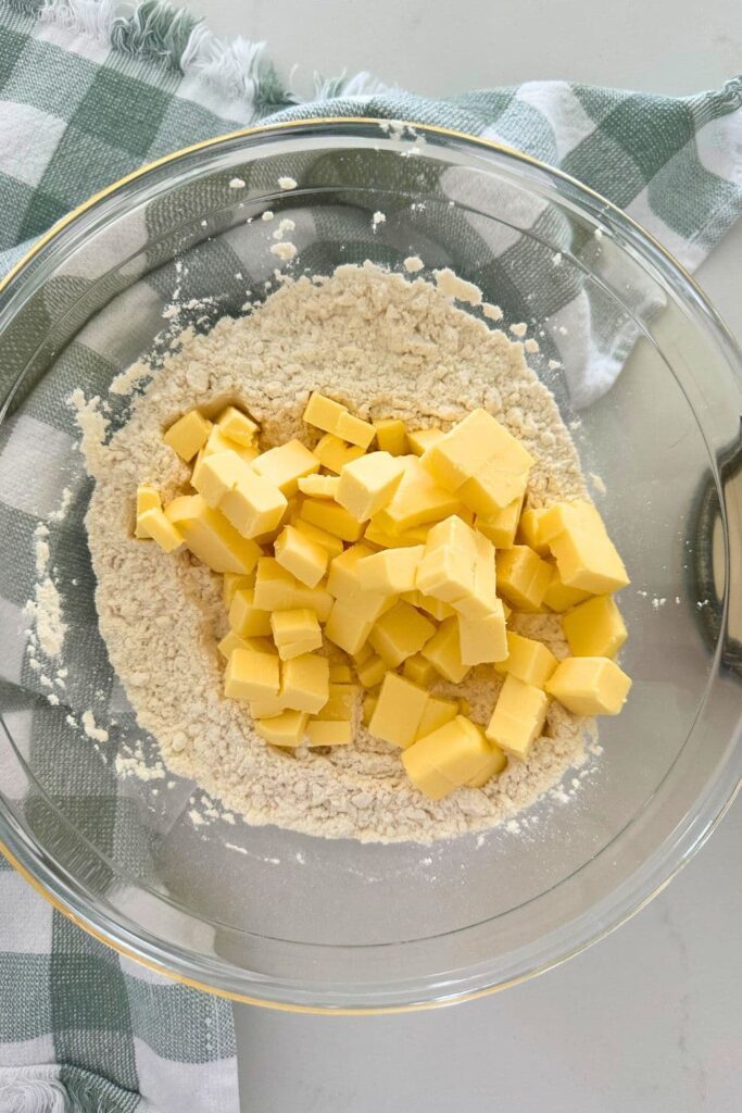 A glass bowl of flour with a heap of cubed butter sitting on top.