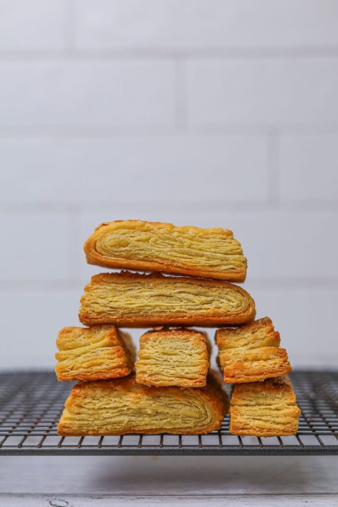 Strips of sourdough puff pastry that have been baked and then stacked up on a cooling rack so you can see the flaky layers made from laminating the butter.