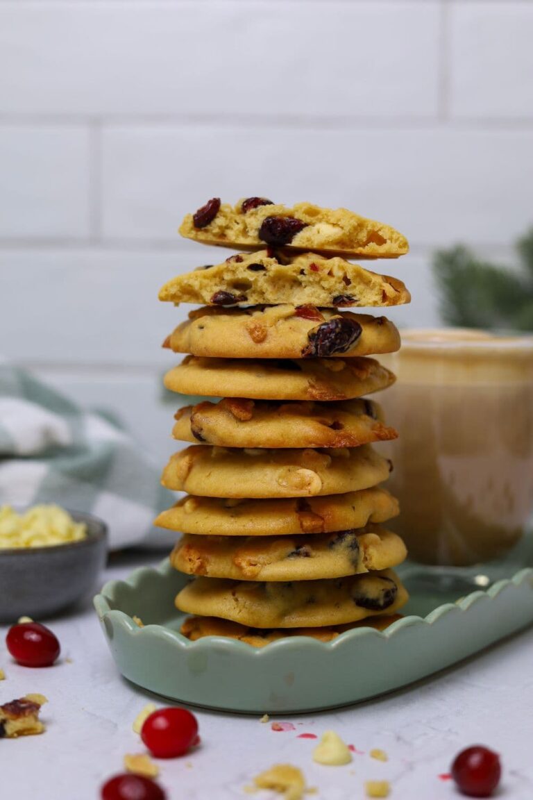 A pile of sourdough cranberry white chocolate cookies stacked up on top of each other. The cookie on the top has been broken in half so you can see the chewy inside.