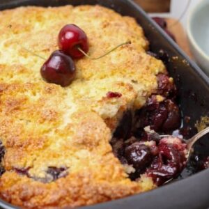 A close up photo of a sourdough cherry cobbler with a scoop taken out so you can see the juicy cherries inside.