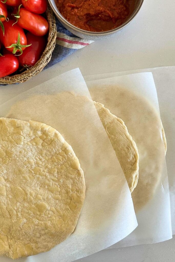 4 sourdough discard pizza bases separated by pieces of parchment paper.