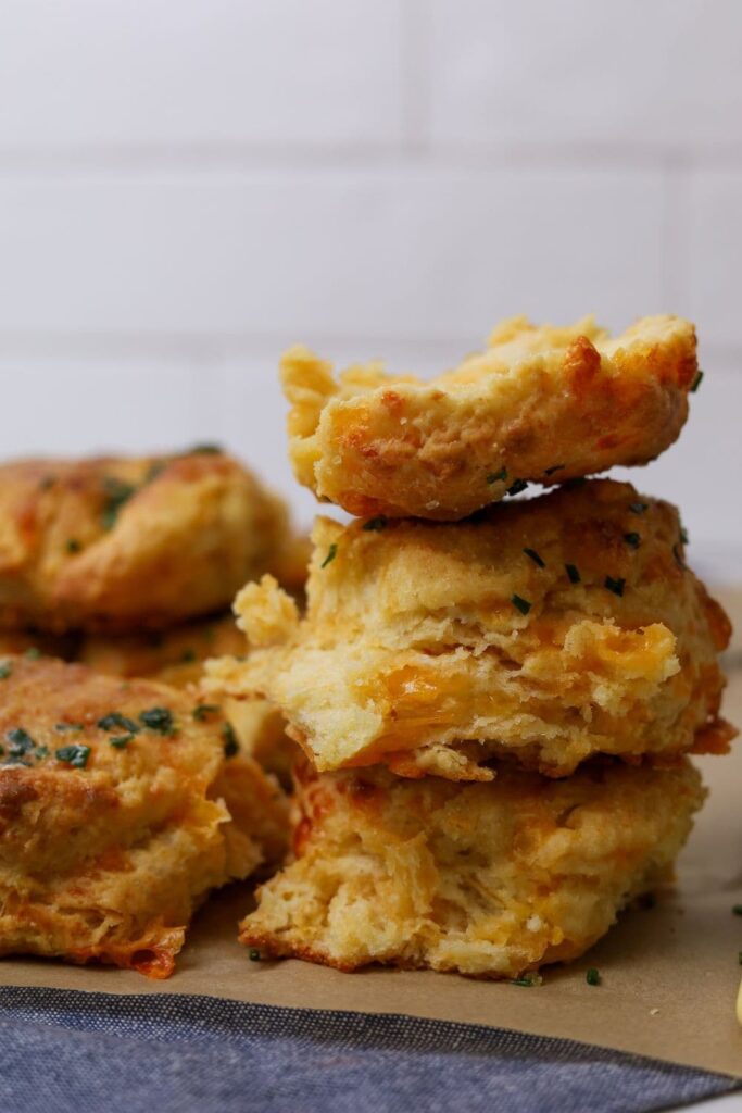 A stack of sourdough cheddar biscuits photographed side on so you can see the flakey layers and the cheesy chunks inside.