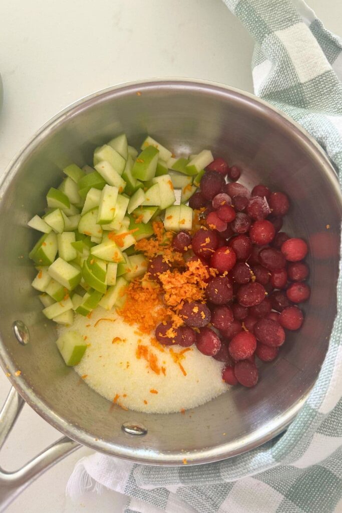 A saucepan containing cranberries, diced green apple, white sugar and orange zest.