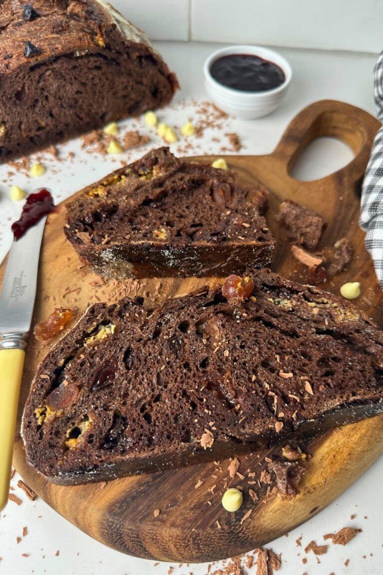 Two slices of sourdough chocolate cherry bread laid out on a wooden serving board. You can see the rest of the loaf in the background.