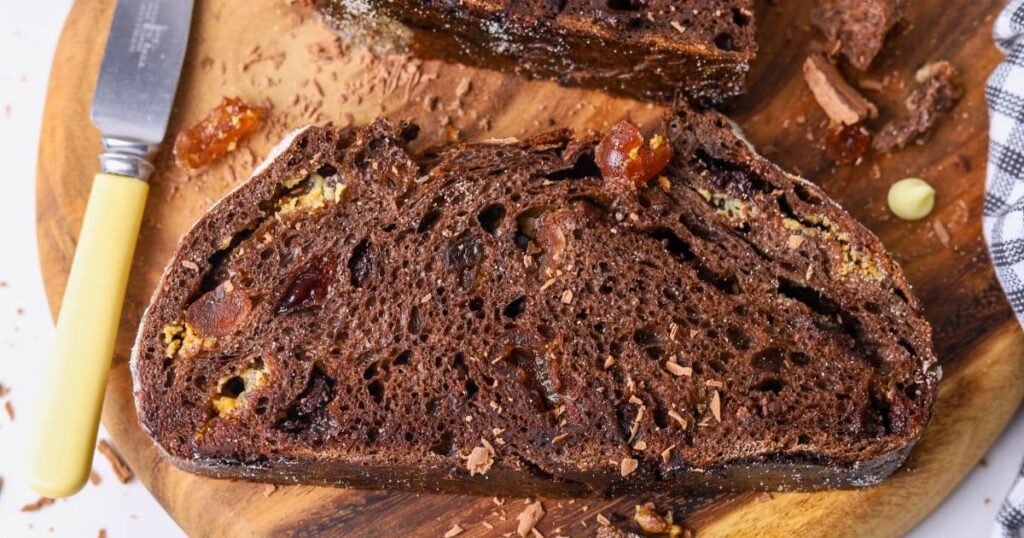 A slice of chocolate cherry sourdough bread laid out horizontally on a round wooden board.