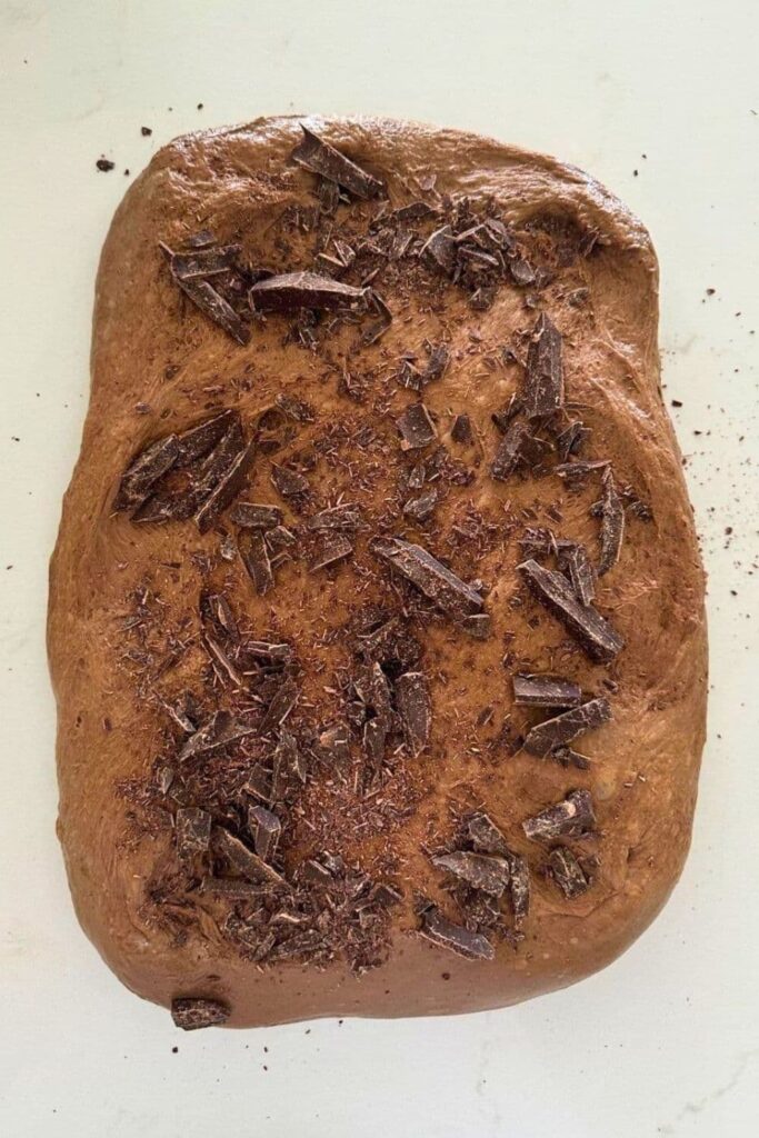 A rectangle of chocolate sourdough laid out on the counter and topped with chunks of chocolate sprinkled over the top of the dough.