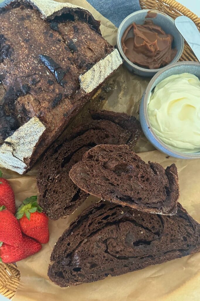 A loaf of sourdough chocolate bread that has been sliced and laid out so you can see the rich interior. There is also some whipped cream and berries in the display.